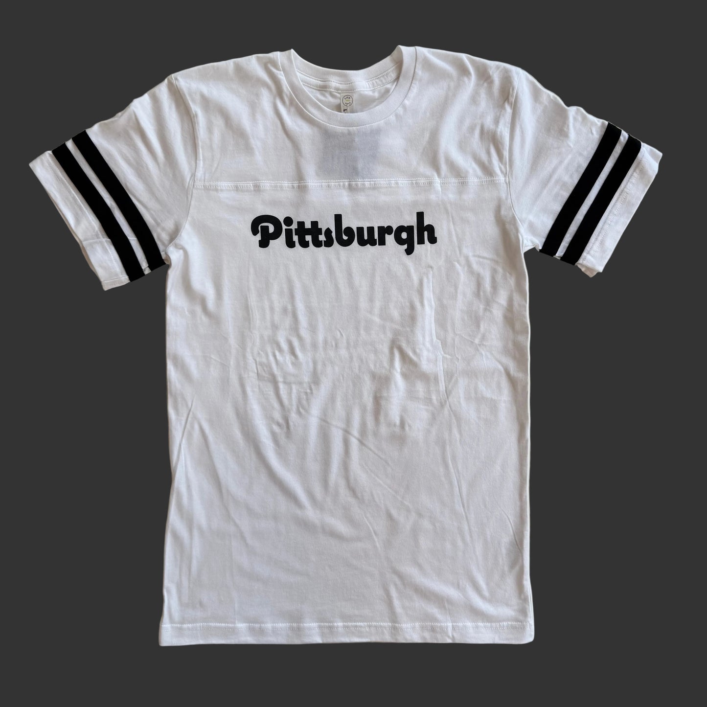 White t-shirt with 'Pittsburgh' text on a wooden surface