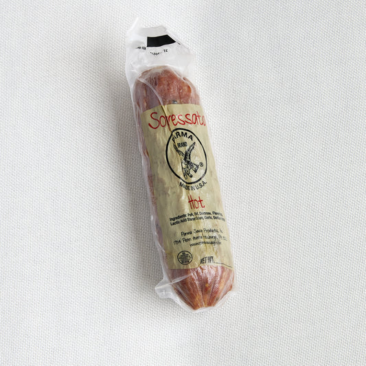 A packaged soprssata, specifically from Parma Sausage, sealed in a clear plastic wrapper with a beige paper label, placed on a textured white fabric background.