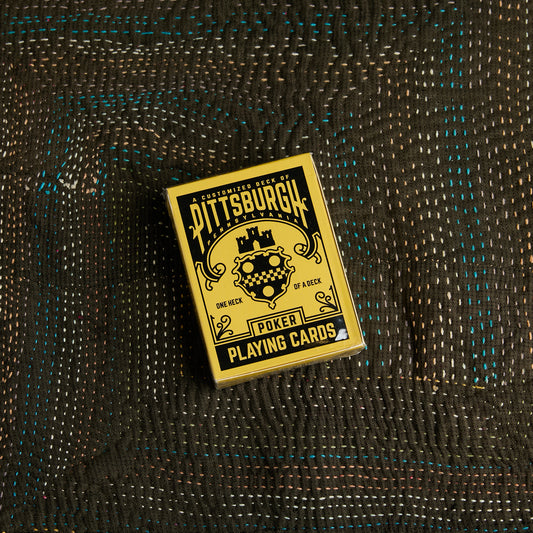 A deck of Pittsburgh Poker Playing Cards in a gold and black box, placed on a dark woven fabric background.