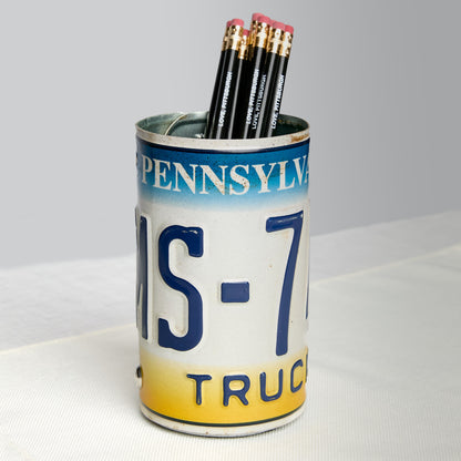 A novelty pencil holder shaped like a vintage Pennsylvania license plate truck plate, filled with four black pencils, set on a white textured surface against a light gray background.