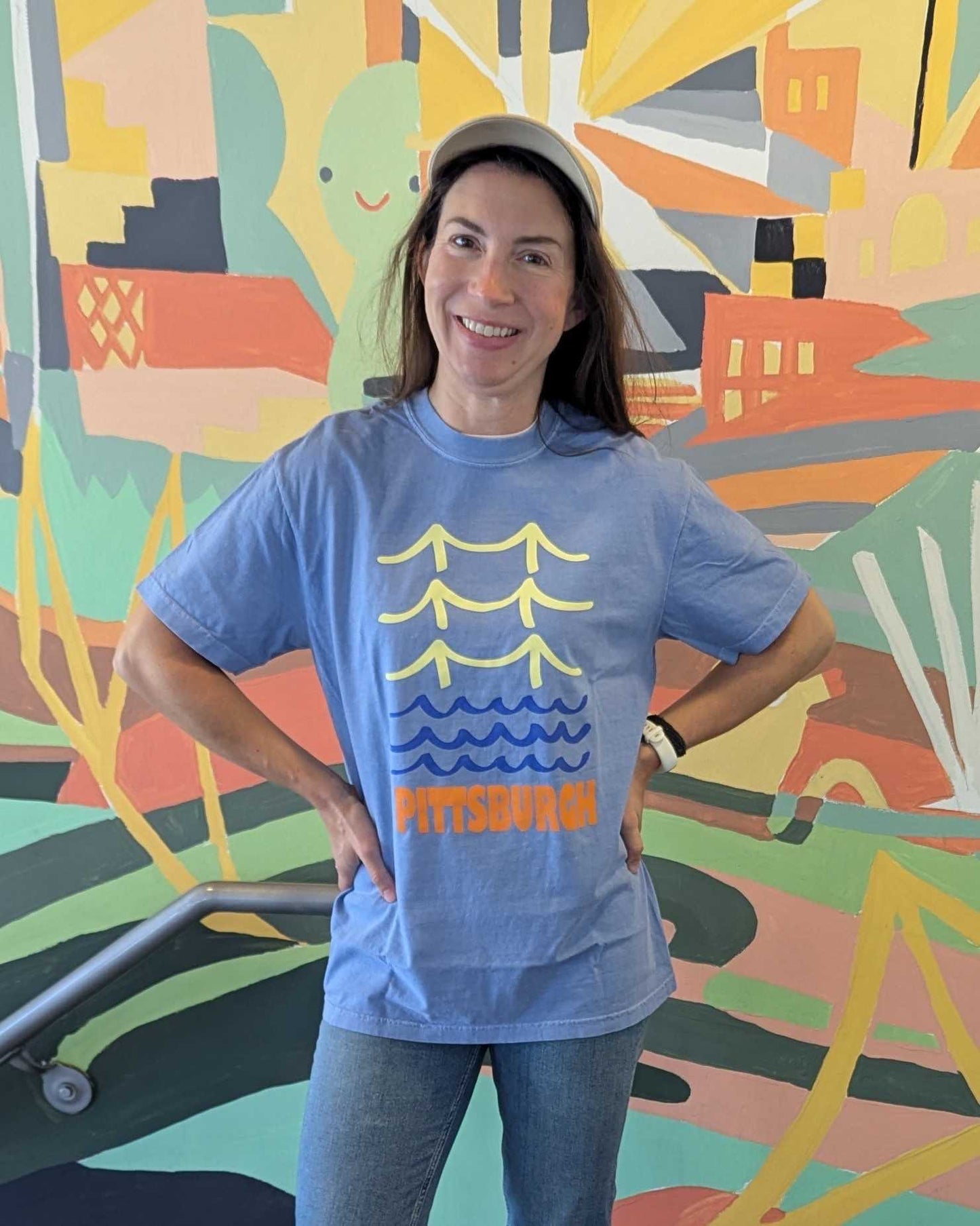 Person wearing a blue t-shirt with a graphic design in front of a colorful mural.