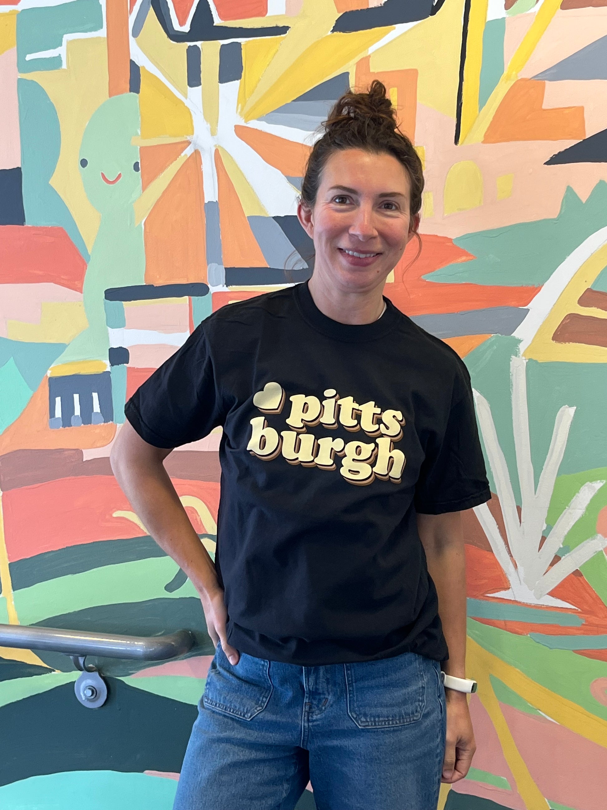 Person wearing a black t-shirt with 'Pittsburgh' text in front of a colorful mural.