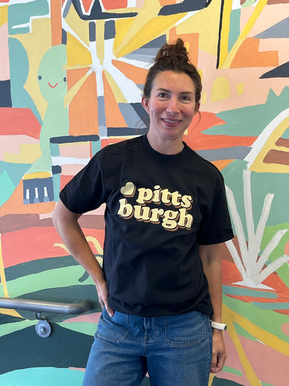 Person wearing a black t-shirt with 'Pittsburgh' text in front of a colorful mural.