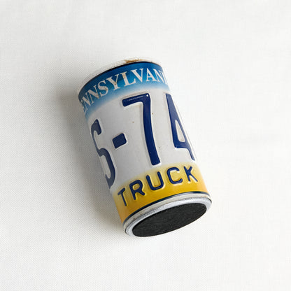A novelty magnet shaped like a vintage Pennsylvania license plate for a truck, featuring the text 'PENNSYLVANIA', '6-74', and 'TRUCK' in blue and yellow on a white background, photographed on a white textured surface.