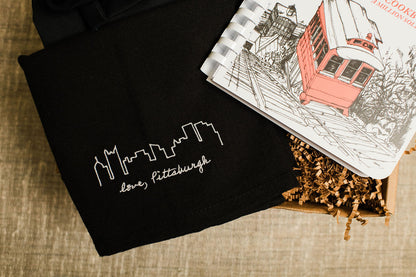 Black tote bag with 'love, Pittsburgh' text and a book on a textured surface