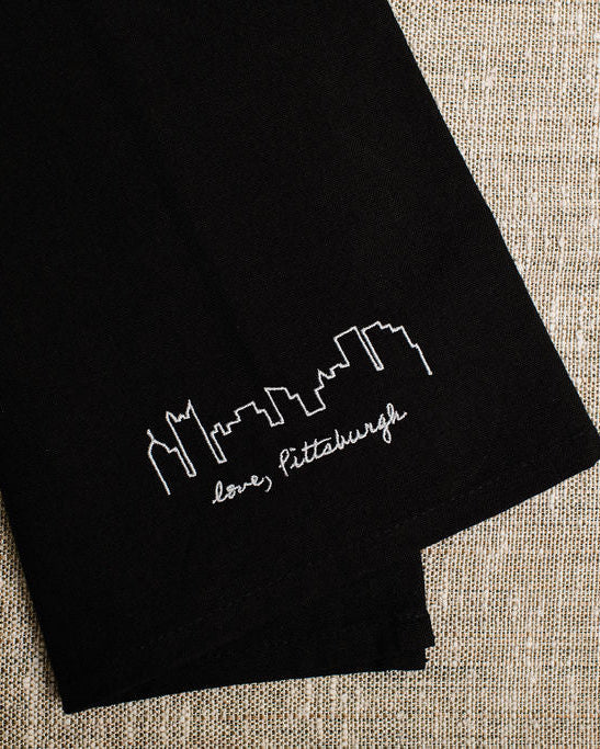 Black napkin with white skyline design and 'love Pittsburgh' text on a beige fabric background