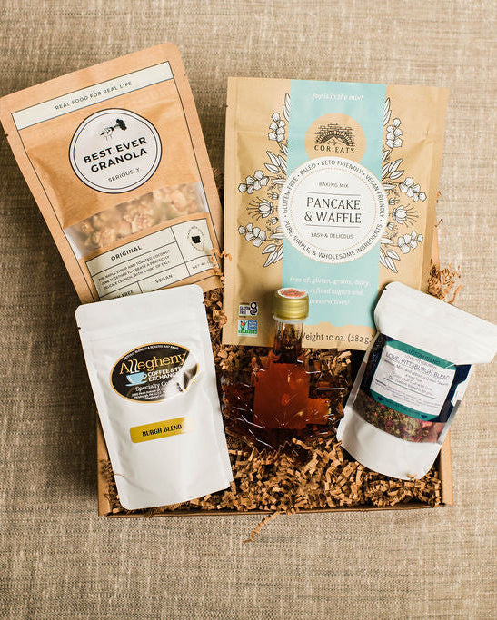 Gift basket with coffee, syrup, and granola on a textured surface