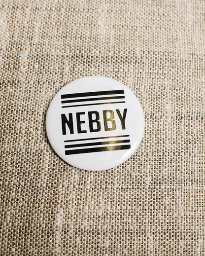 Round white magnet with 'NEBBY' text on a textured beige background