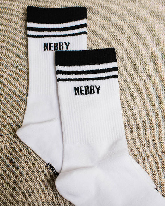 White socks with black stripes and 'NEBBY' branding on a textured beige surface