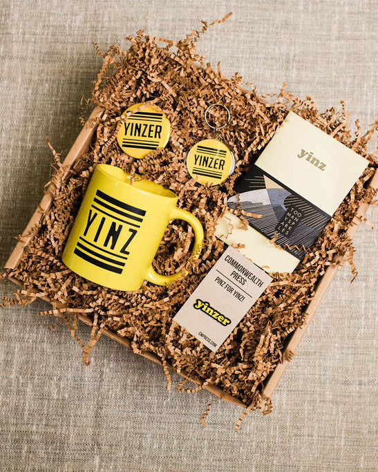 Gift set with a yellow mug, cards, and a box labeled 'yinz' on a textured surface.