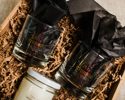 Two rocks glasses and a love candle on a textured surface with black paper