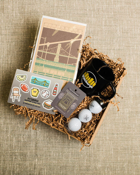 Collection of gifts including golf balls, stickers, bookmark, mug, and card on a textured brown surface
