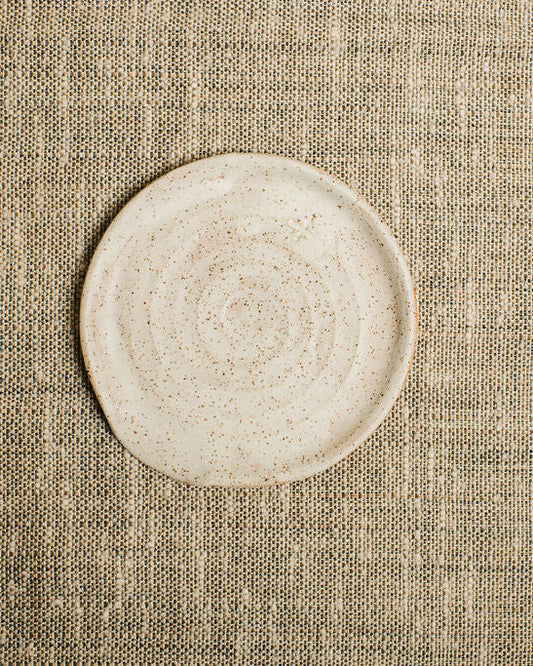 Round beige ceramic spoon rest on a textured beige fabric background