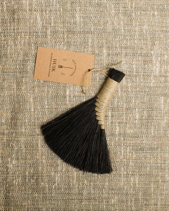 Black brush broom  with beige trim on a textured beige fabric background