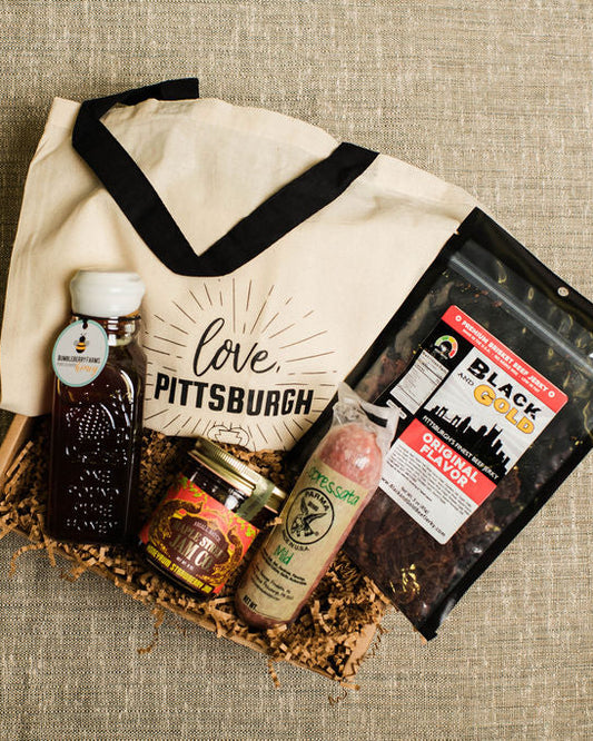 Gift basket with 'Love Pittsburgh' tote bag, snacks, and trears on a textured surface