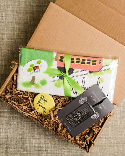 Open cardboard gift box with incline theme towel, ornament, and magnet on a textured surface