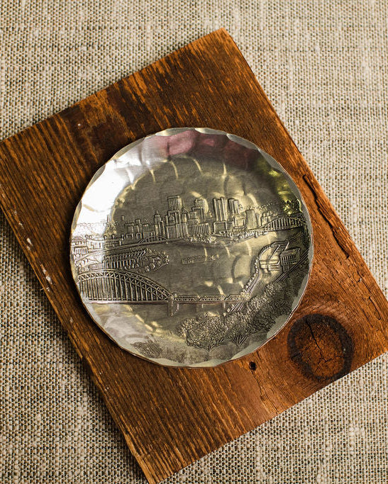 aluminum coaster with pittsburgh skyline on a wooden block with a textured beige background