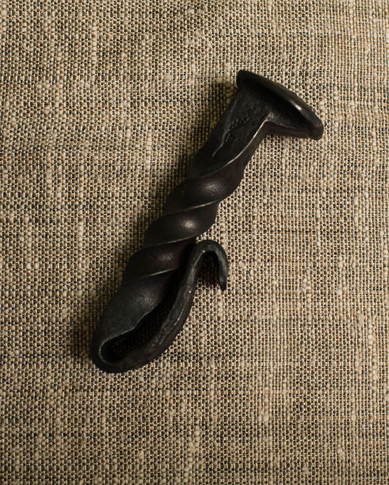 Black twisted railroad spike bottle opener on a beige textured fabric background