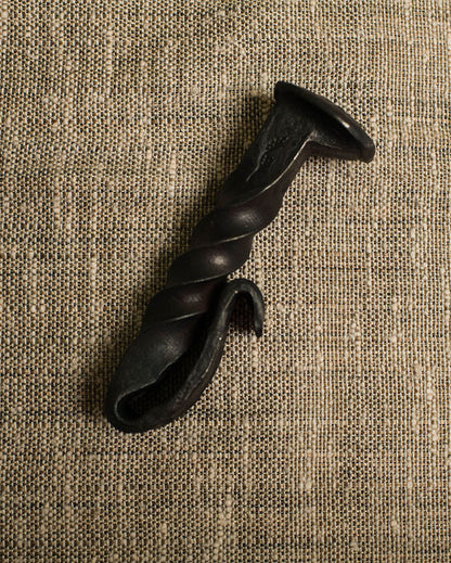 Black twisted railroad spike bottle opener on a beige textured fabric background