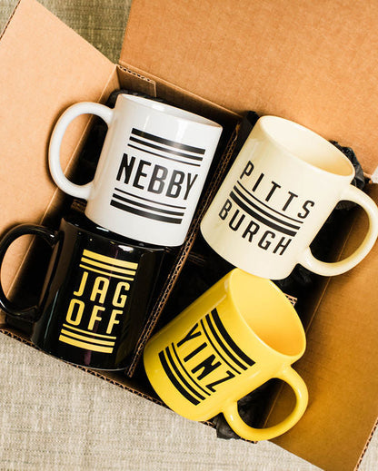 Four pittsburgh mugs with text designs in a box on a textured surface