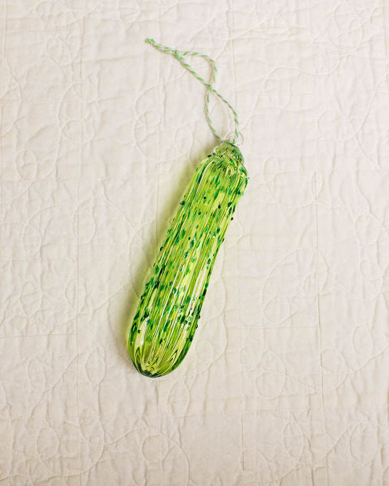 Green glass pickle ornament on a beige textured background