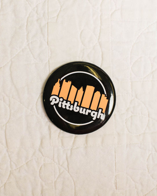 Round magnet with 'Pittsburgh' text and skyline design on a textured white background