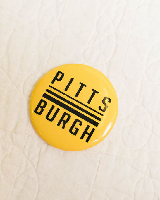 Yellow magnet with 'Pittsburgh' text on a light wood surface