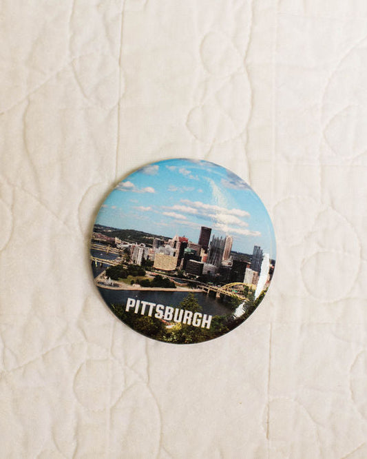 Round magnet with Pittsburgh skyline on a textured white surface