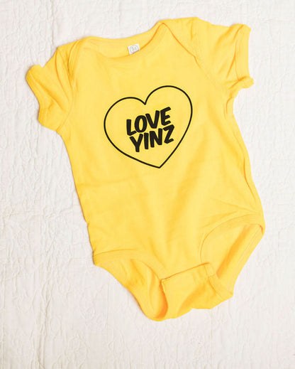 Yellow baby onesie with a heart-shaped  love yinz logo on a white background