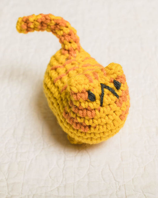 Crocheted yellow and orange cat toy on a textured white surface