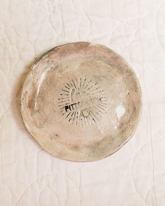 Round ceramic dish with textured surface and pittsburgh logo stamp on a beige background