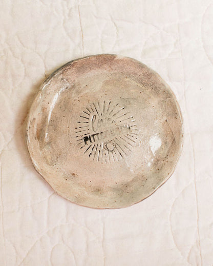 Round ceramic dish with textured surface and pittsburgh logo stamp on a beige background