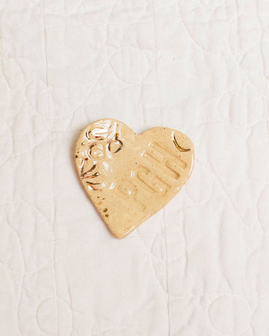 Gold accent heart-shaped trinket dish with PGH stamp on a textured white surface