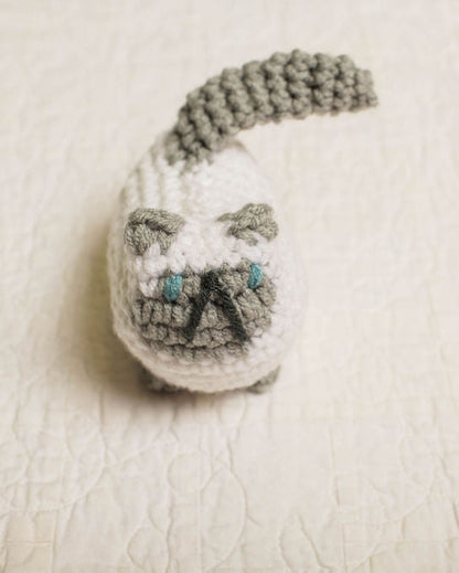 Small crocheted white and grey cat on a textured beige surface
