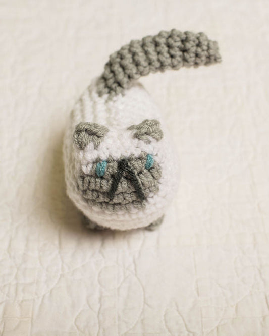 Small crocheted white and grey cat on a textured beige surface