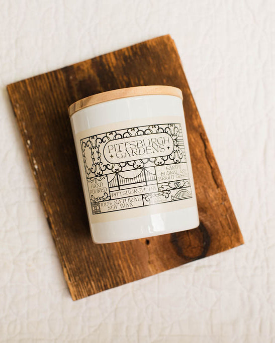 Candle with a decorative pittsburgh gardens label on a wooden coaster