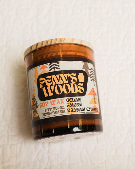 Scented candle jar labeled 'Penn's Woods' on a textured white surface