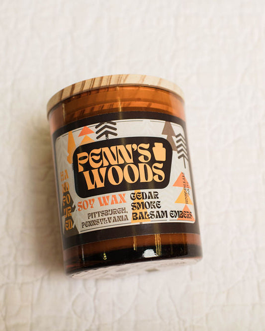 Scented candle jar labeled 'Penn's Woods' on a textured white surface