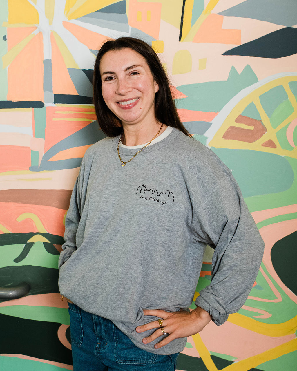 Woman wearing a gray sweatshirt with text standing in front of a colorful abstract wall.