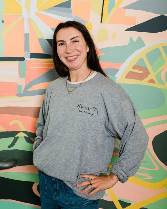 Woman wearing a gray sweatshirt with text standing in front of a colorful abstract wall.