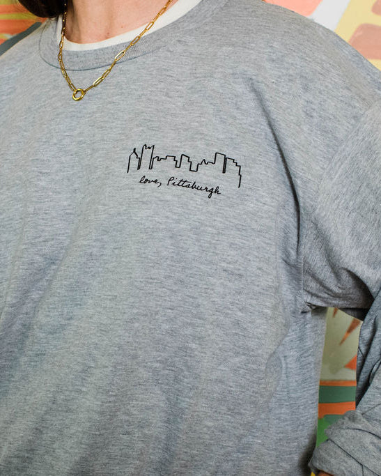 Person wearing a gray sweatshirt with a logo in front of a colorful abstract background