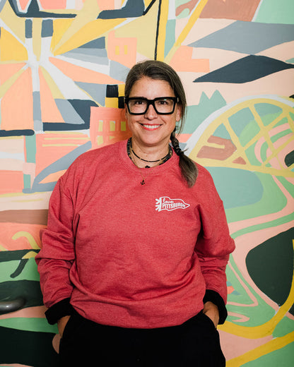 Person wearing a red sweatshirt with a logo in front of a colorful abstract mural.