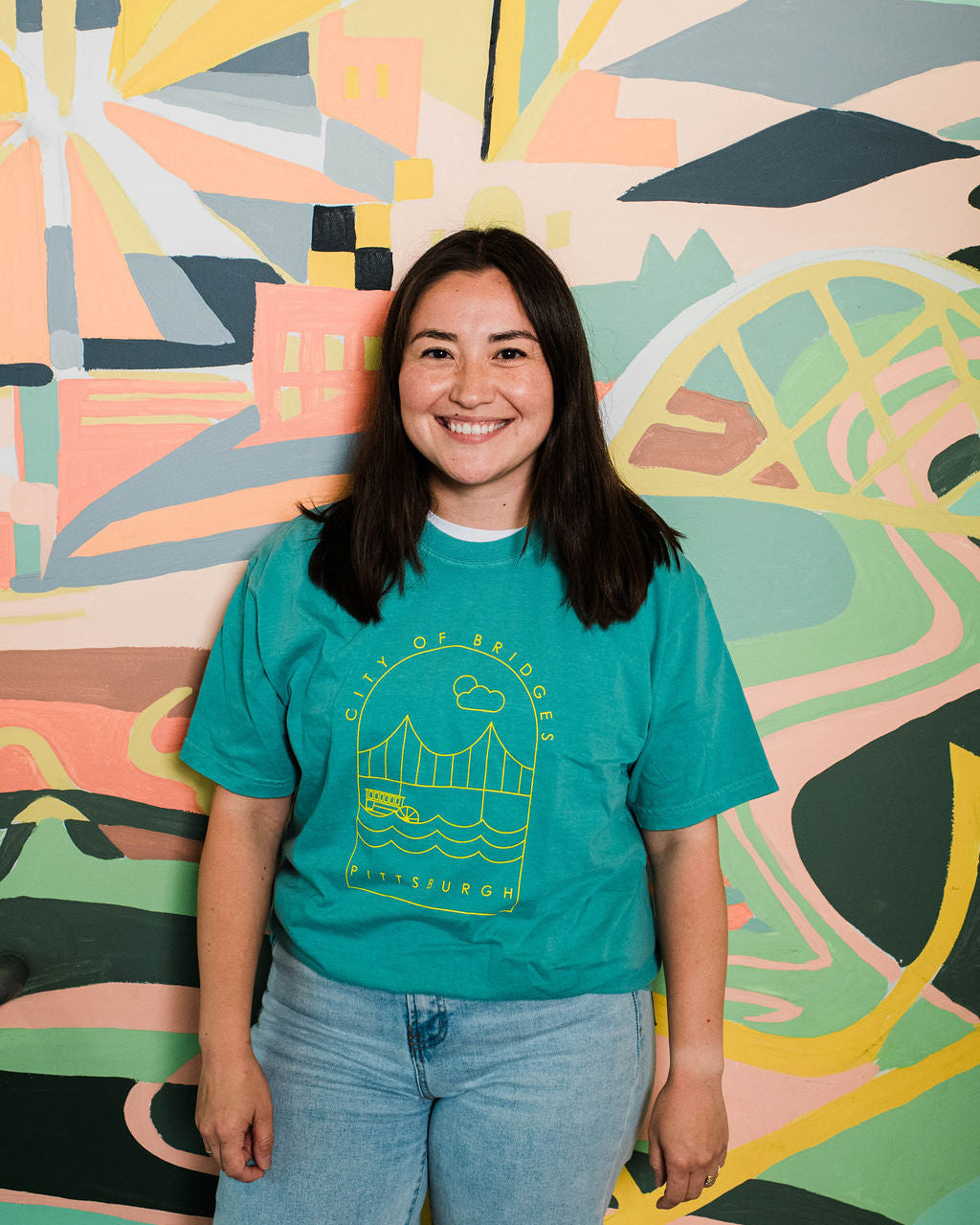 Person wearing a teal t-shirt with a graphic design, standing in front of a colorful abstract wall.