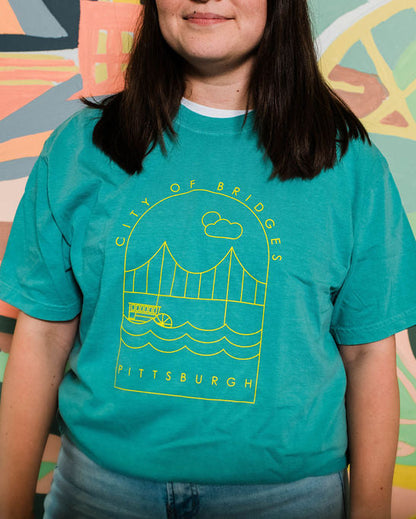 Person wearing a teal t-shirt with a graphic design in front of a colorful mural.