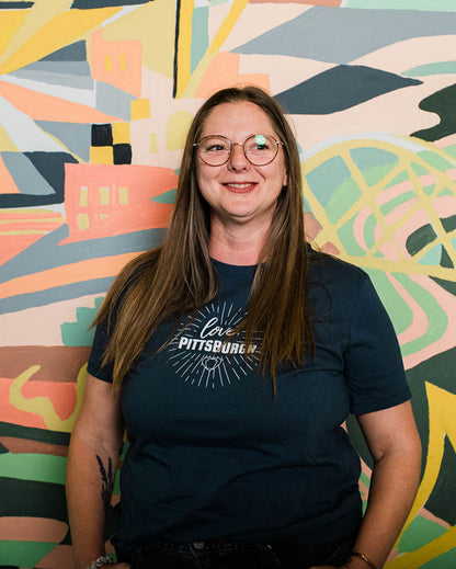 Person wearing a dark blue t-shirt with text standing in front of a colorful abstract mural.