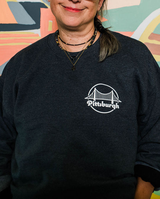 Person wearing a black sweatshirt with 'Pittsburgh' print in front of a colorful mural.