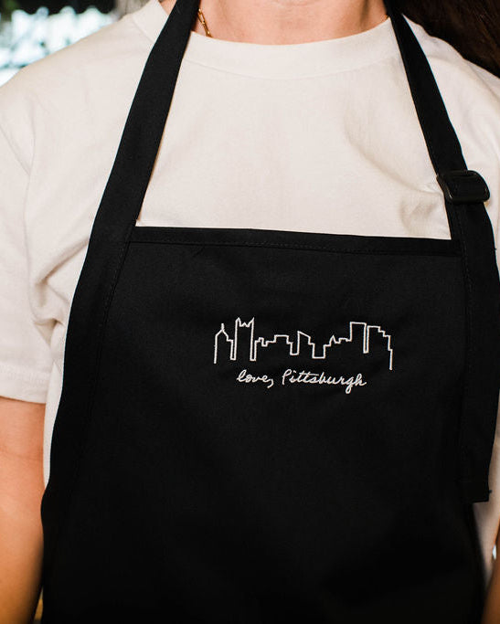 Person wearing a black apron with a white design and text, standing indoors.