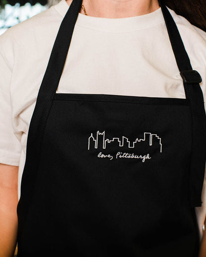 Person wearing a black apron with a white design and text, standing indoors.