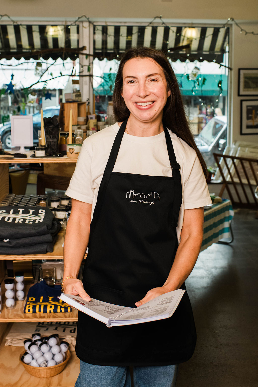 Person wearing a black apron with a logo, holding a piece of paper in a store setting.