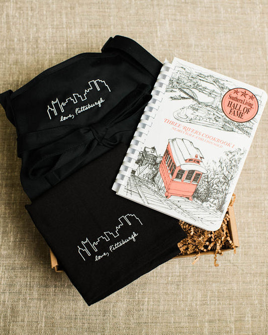 Two black t-shirts with white text and a notebook on a beige fabric background